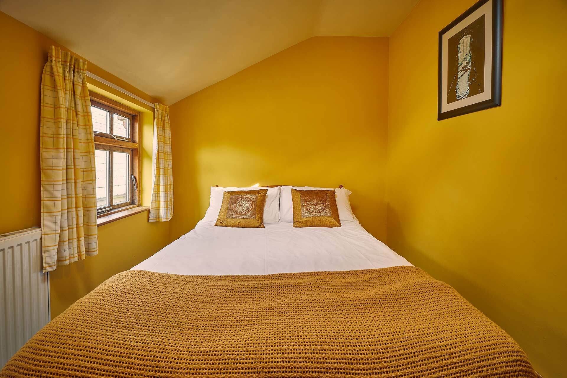 A room with a bed, yellow walls, a window with curtains, and a framed picture on the wall.