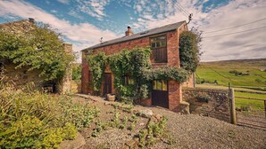 A rustic brick house with ivy-covered walls, a gravel driveway, and a rural landscape in the background. - Host Stay The Red Brick Barn (Bishop Auckland)