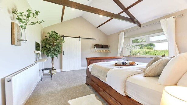 A bedroom with a wooden bed, a bedside table with a tray of breakfast, a potted plant, and a view of greenery outside. - Host Stay The Pepper Pot (Alnwick)
