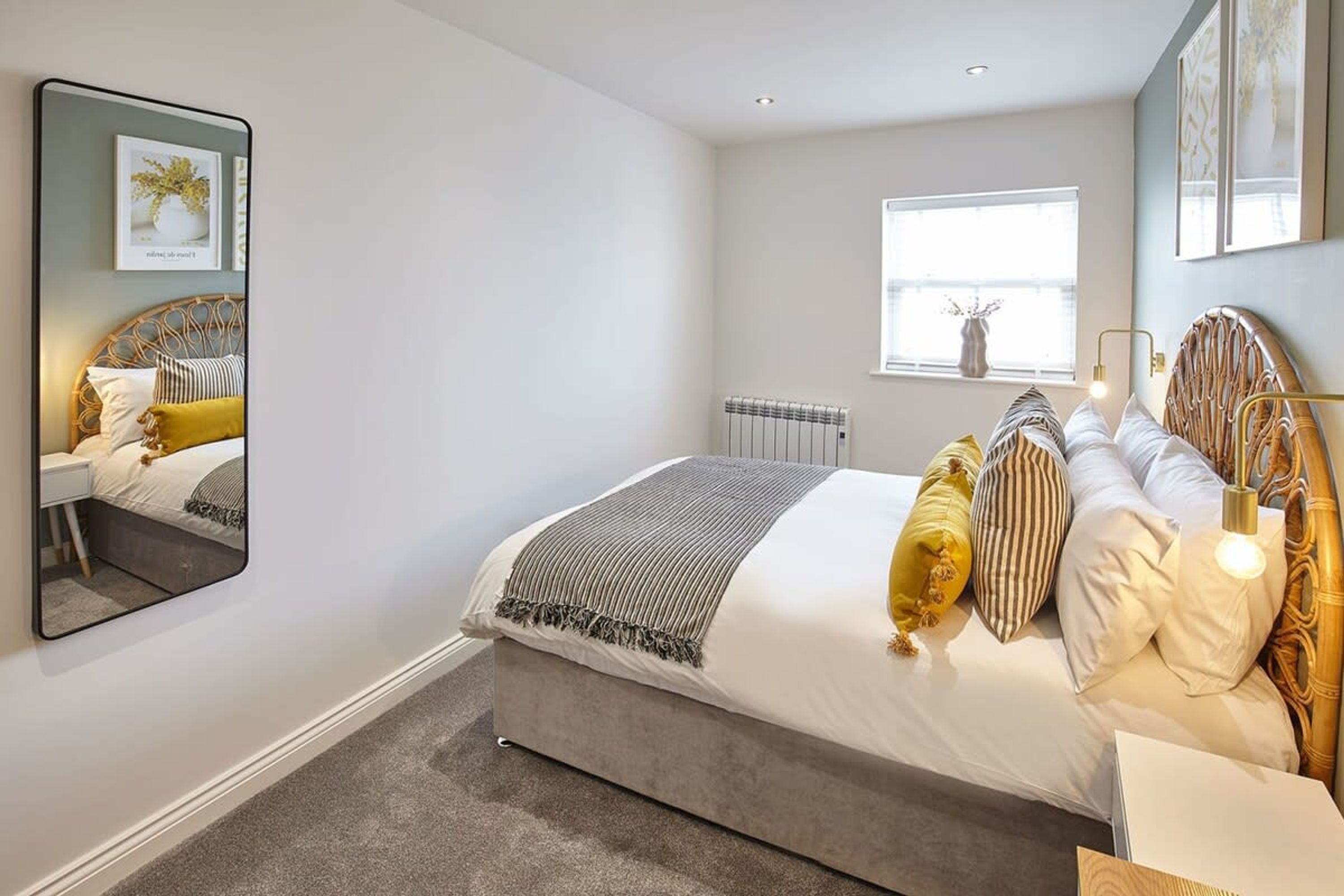 A modern bedroom with a large bed, a bedside table, a mirror, and a window with a view of the outside.