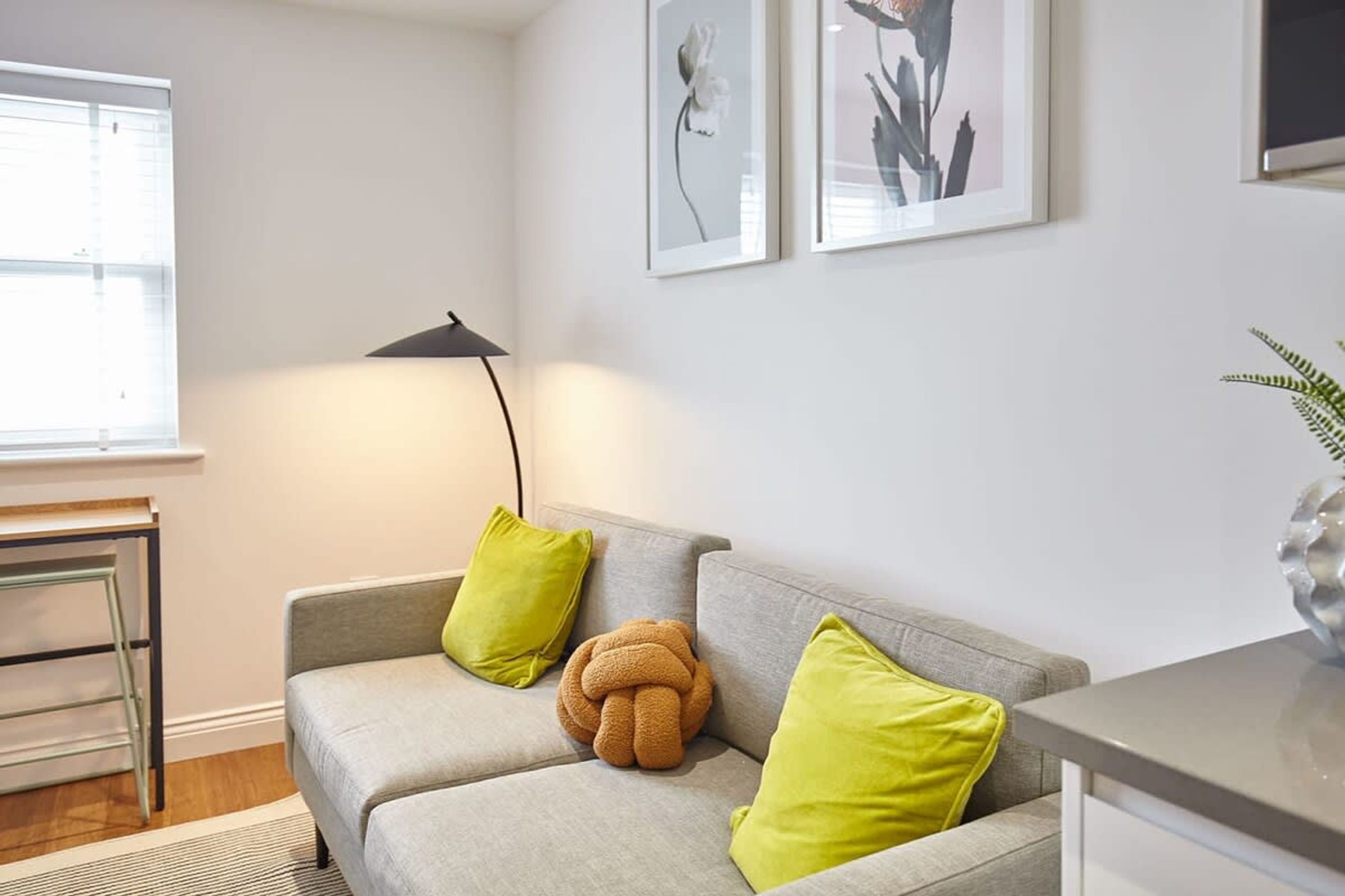 A modern living room with a grey sofa, two green cushions, a unique brown decorative item, and a black floor lamp.