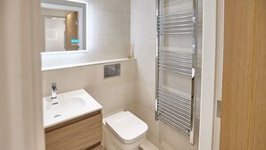 A modern bathroom with a white sink, wooden vanity, a toilet, and a glass shower enclosure. - Host Stay Sandcastles Apartment (Whitby)