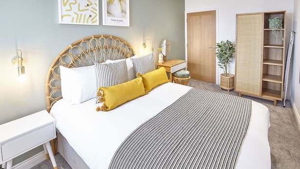A bedroom with a large bed, bedside tables, a wardrobe, and wall art. - Host Stay Sandcastles Apartment (Whitby)