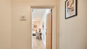 A hallway leading to a bedroom with a bed, a desk, and a chair. There is a sign on the wall and a framed picture. - Host Stay Studio Pod 2 (Saltburn-by-the-Sea)