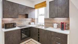 A modern kitchen with dark cabinets, a microwave, oven, and a coffee maker. - Host Stay Studio Pod 2 (Saltburn-by-the-Sea)