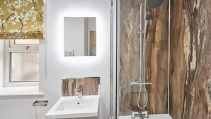 A bathroom with a white sink, a mirror, a shower with a glass enclosure, and a wooden wall. - Host Stay Studio Pod 2 (Saltburn-by-the-Sea)