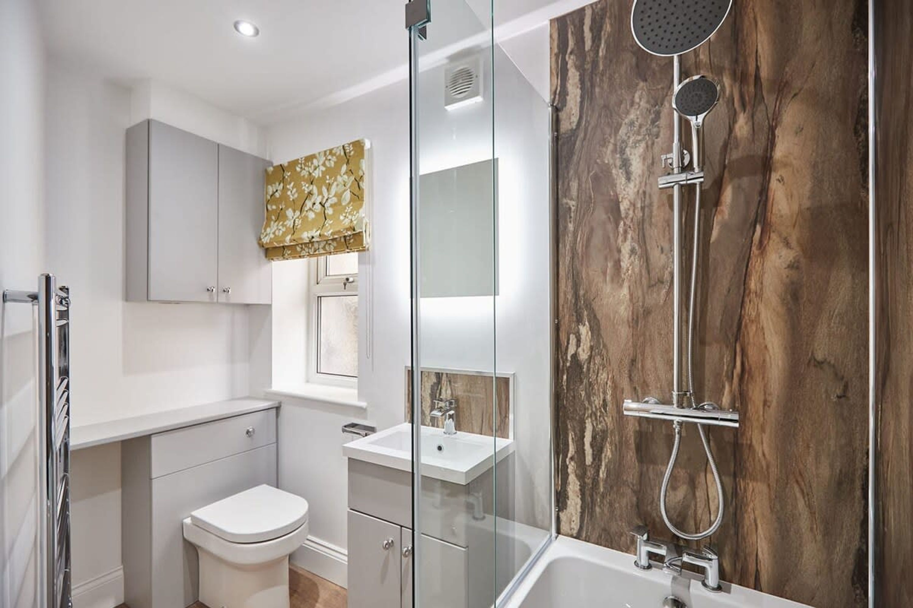 A modern bathroom with a glass shower enclosure, a white toilet, a vanity with a mirror, and a wooden accent wall.