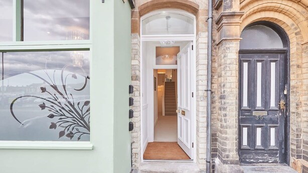 A building entrance with a door, a window with a floral design, and a view of a cityscape. - Host Stay Studio Pod 2 (Saltburn-by-the-Sea)