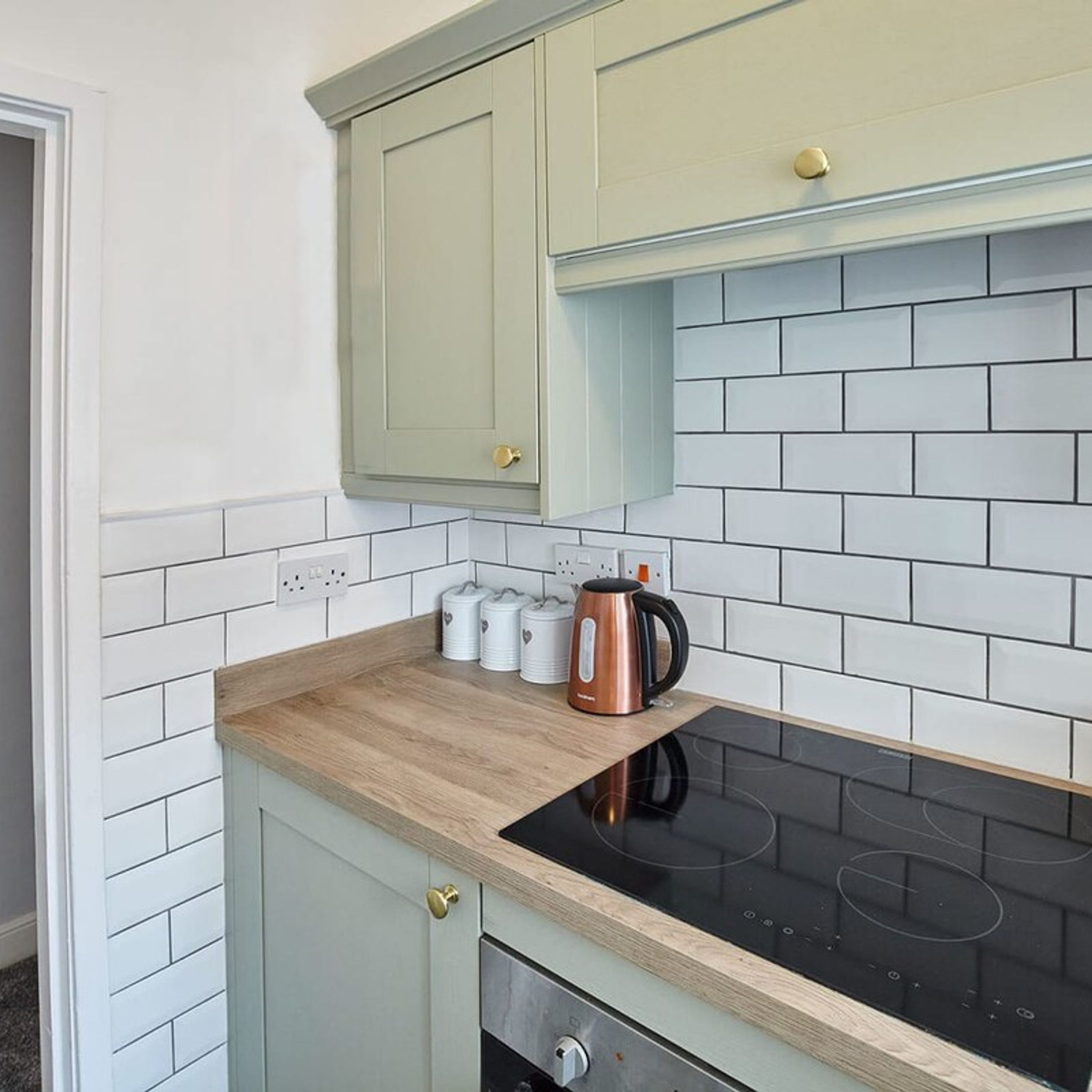 Una cocina con azulejos blancos tipo metro, una encimera de madera y una placa de inducción negra.