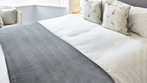 A neatly made bed with a grey blanket, two pillows with a bird pattern, and a window with blinds. - Host Stay Cobblestones (Redcar)