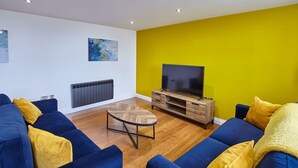 Uma sala de estar moderna com um sofá azul, uma mesa de centro de madeira e uma televisão de tela plana em um suporte de madeira.