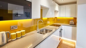 Uma cozinha moderna com armários brancos, pia de aço inoxidável e painel de parede amarelo.