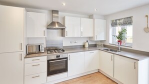 A modern kitchen with white cabinets, stainless steel appliances, and a window with a plant.