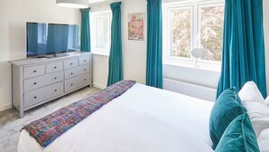 A bedroom with a bed, a dresser, a television, and a window with curtains.
