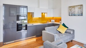 A modern kitchen with grey cabinets, a grey sofa with a yellow pillow, and a painting on the wall.