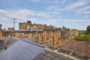 A historic stone castle with multiple towers and battlements, viewed from a rooftop with solar panels. - Host Stay Muggles Mews (Alnwick)