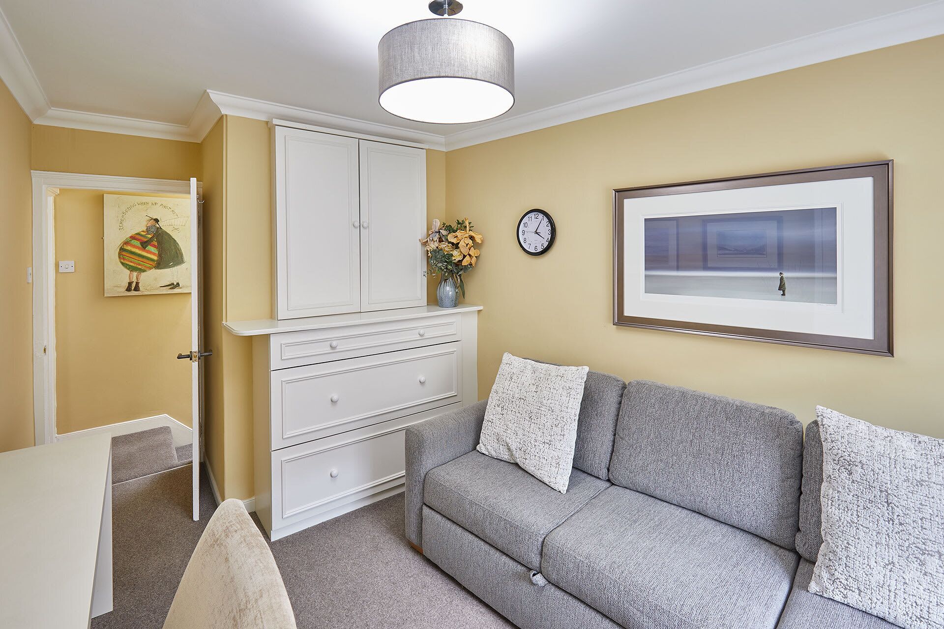 A room with a grey sofa, white dresser, and a painting on the wall.