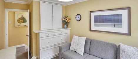 A room with a grey sofa, white dresser, and a painting on the wall.