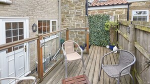 A wooden deck with two wicker chairs and a table, surrounded by a stone wall and a wooden fence. - Host Stay Honeysuckle Cottage (Saltburn-by-the-Sea)