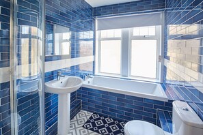 Une salle de bain avec des carreaux bleus, un lavabo blanc, une baignoire et des toilettes.