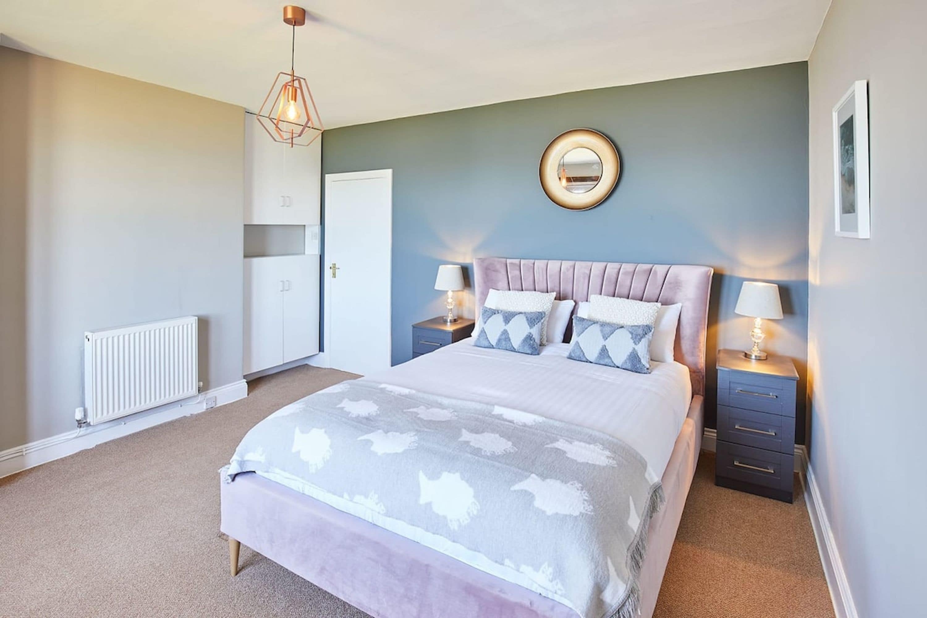 A bedroom with a bed, bedside tables, a mirror, and a radiator.