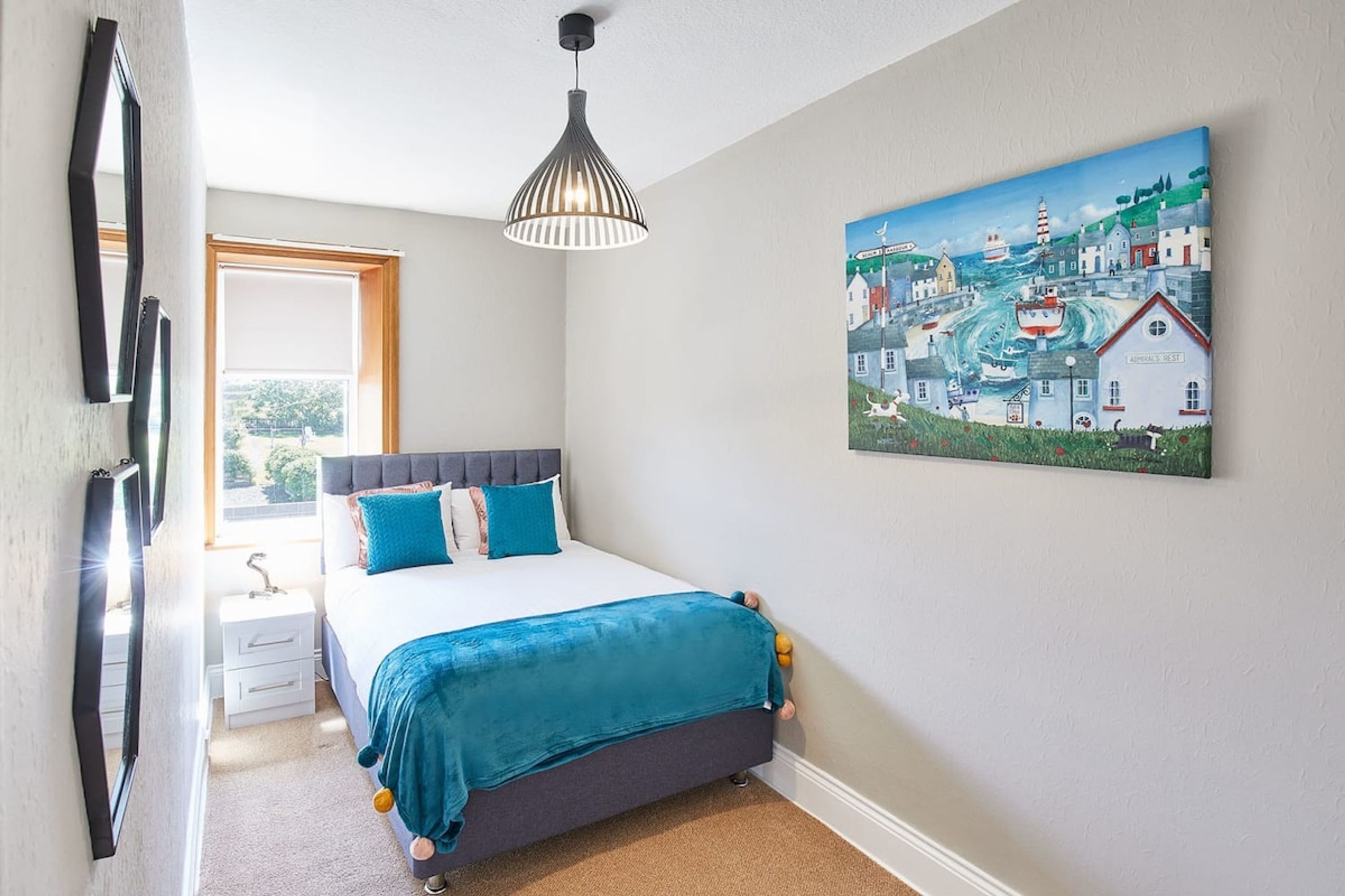 A bedroom with a bed, a bedside table, a nightstand, a window, and a painting on the wall.