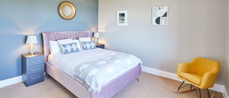 A bedroom with a bed, bedside tables, a chair, and wall art.