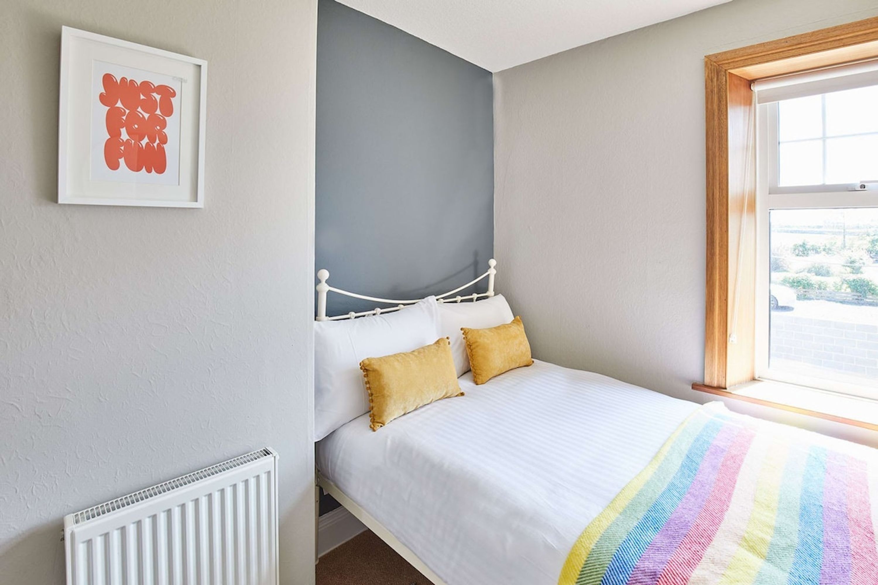 A bedroom with a bed, a radiator, a framed artwork, and a window.