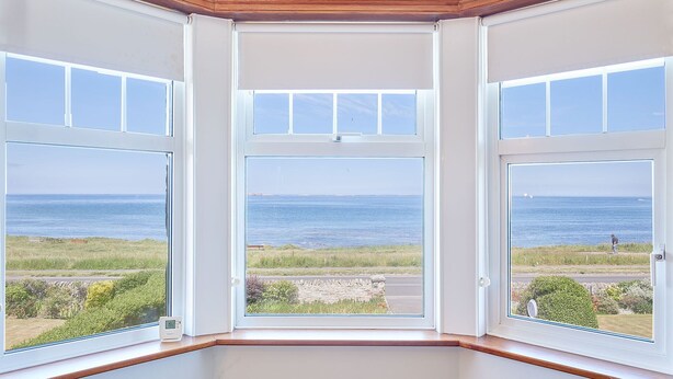 A bay window with a view of the sea and a grassy area. - Host Stay The Puffins Nest (Seahouses)