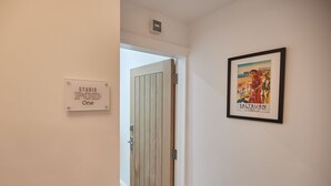 Um corredor com uma porta de madeira com a placa “STUDIO POD One” e um cartaz emoldurado de “Saltburn e Marksby-by-the-Sea” na parede.