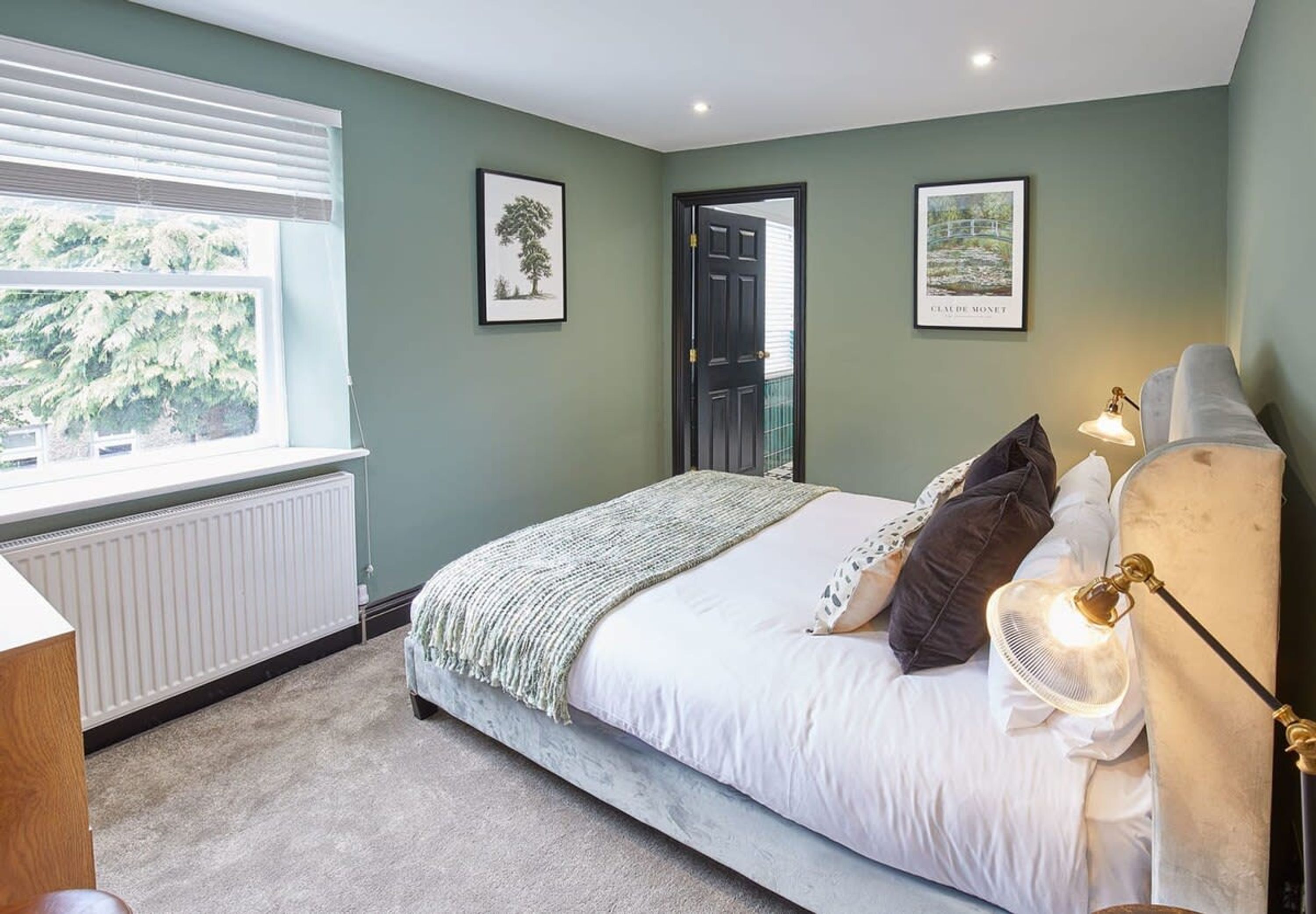 A bedroom with a bed, a radiator, a window, and two framed pictures on the wall.