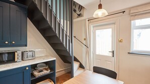 A kitchen with dark blue cabinets, a wooden table, and a staircase leading to a door. - Host Stay The Railman s House (York)