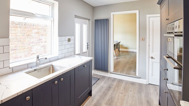 A modern kitchen with dark cabinets, a white countertop, and a brick wall. - Host Stay The Old Fireman s House (Saltburn-by-the-Sea)