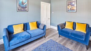 A room with two blue sofas with yellow cushions, a wooden floor, and two framed artworks on the walls. - Host Stay The Old Fireman s House (Saltburn-by-the-Sea)