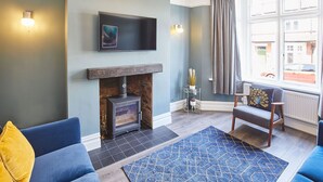 A living room with a fireplace, a blue sofa, a patterned rug, and a window with curtains. - Host Stay The Old Fireman s House (Saltburn-by-the-Sea)