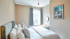 A bedroom with a bed, a bedside table, a window with curtains, a wall-mounted mirror, and a framed picture. - Host Stay The Old Fireman s House (Saltburn-by-the-Sea)