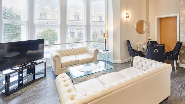 A modern living room with a large flat-screen TV, two white sofas, a glass coffee table, and a dining area with a round table and chairs. - Host Stay Three Bays (Scarborough)