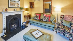 Un salon avec une cheminée, un canapé, un pouf et un fauteuil à motifs floraux.