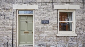 Un bâtiment en pierre avec une porte verte et une fenêtre. Une enseigne au-dessus de la fenêtre indique : « Sixpence Cottage ».