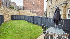 A backyard with a grassy lawn, a metal chair, a table, and a black umbrella. - Host Stay Aynsley Mews (Consett)