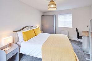 A bedroom with a bed, bedside table, lamp, wardrobe, and a window with blinds.