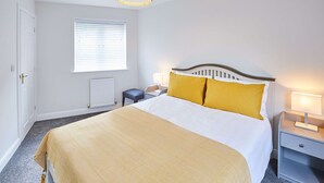 A bedroom with a bed, bedside table, lamp, window, radiator, and a door. - Host Stay Aynsley Mews (Consett)