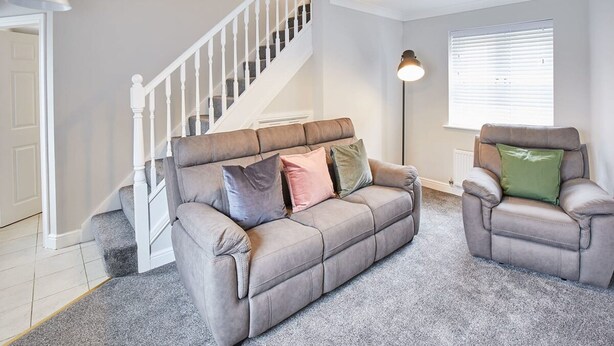 A living room with a grey sofa, a recliner, a staircase, and a window with blinds. - Host Stay Aynsley Mews (Consett)