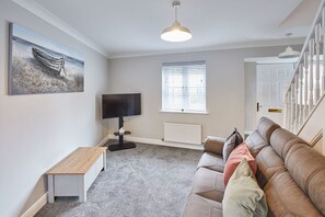 A living room with a sofa, a TV, a painting, a bench, and a window with blinds.