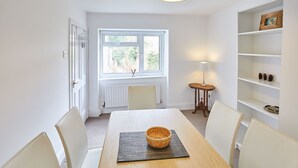 A dining area with a table, chairs, a basket, a lamp, and a shelf with decorative items. - Host Stay The Duck Pond (Durham)