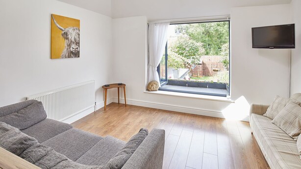 A living room with a large window, a grey sofa, a beige sofa, a painting of a cow, and a flat-screen TV. - Host Stay The Duck Pond (Durham)