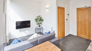 A modern living room with a grey sofa, a wooden coffee table, a mounted TV, and a potted plant. - Host Stay Apartment 2 Queens Court (Scarborough)