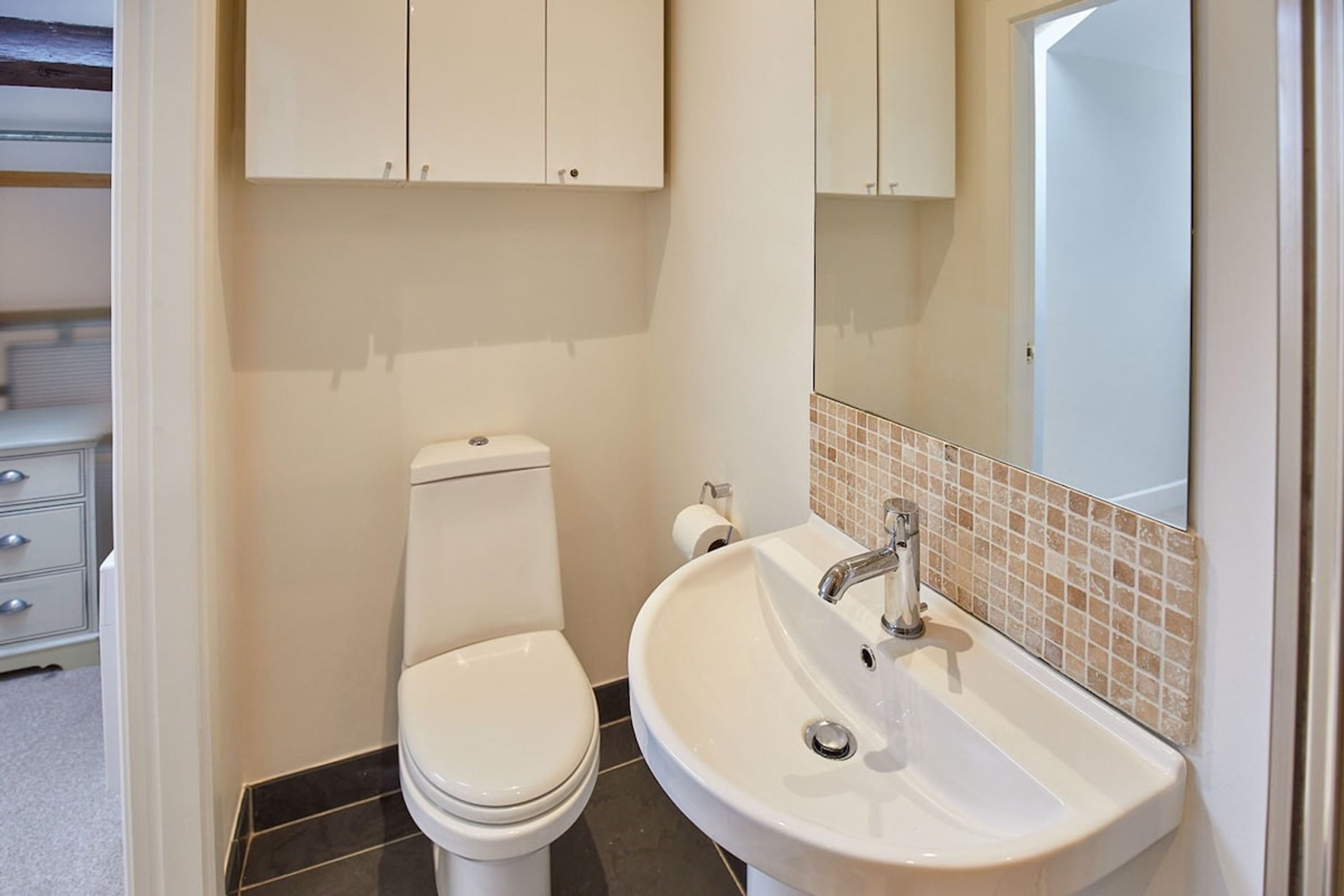 A bathroom with a toilet, sink, and cabinets.