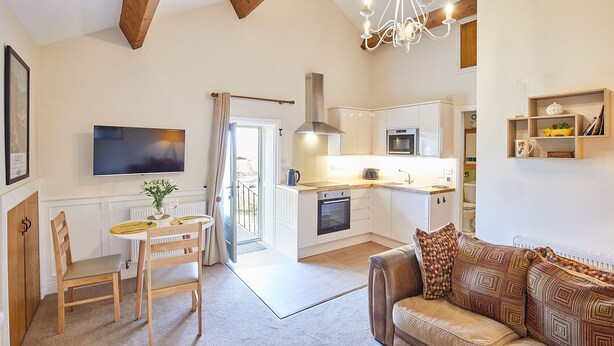 Cozinha moderna com ilha central, sala de jantar com mesa e cadeiras, um sofá e um candelabro.