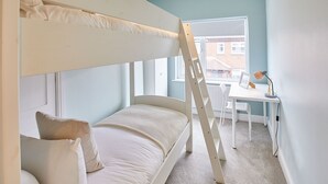 Ein Stockbett mit Schreibtisch und Stuhl, einem Heizkörper und einem Fenster mit Blick auf Gebäude.